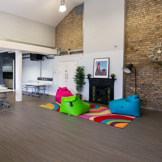 An interior photo of the iD8 Studio at The Digital Hub, with its colourful beanbags, tables and chairs in the background and a green tiled fireplace which is a focal point in the room.