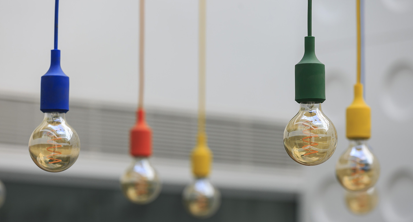Modern light bulbs in primary colours hang in a bright, airy space.