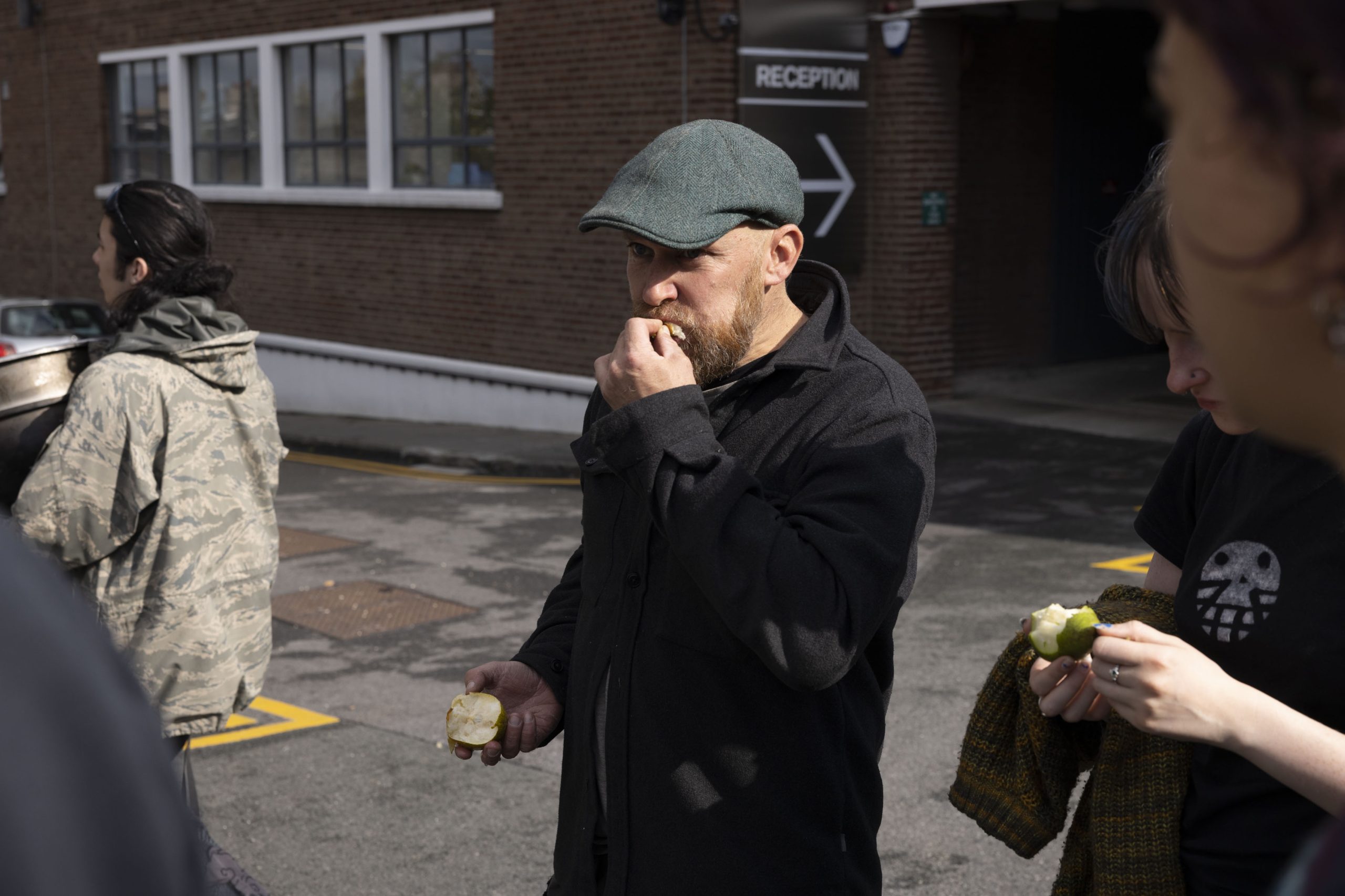 A man wearing a green cap is eating a pear just picked from a tree which is out of shot.