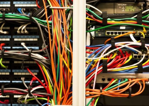 Colorful data network cables in orange, yellow, red, green and blue are plugged into machines stacked one on top of the other.