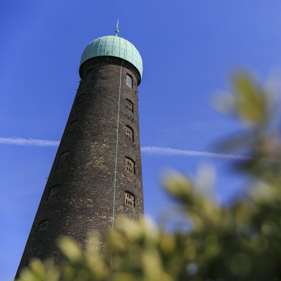 A tall round tower, known as St Patrick's Tower, with its brown bricks and green copper dome against a clear blue sky.